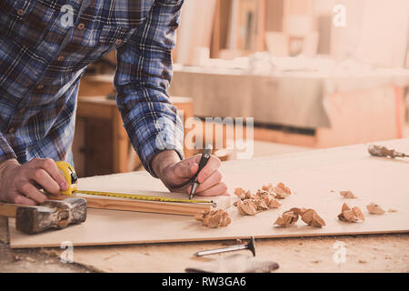 Carpenter working with measure tape, meter or rule taking measures on wood using pencil. Workshop background. Carpenter workbench. Stock Photo
