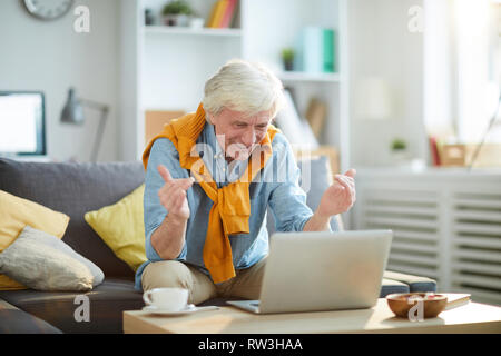 Portrait of contemporary senior man smiling happily while using laptop at home, copy space Stock Photo
