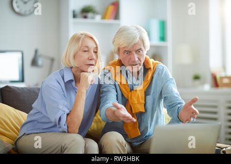 Portrait of shocked senior man looking at computer screen while using laptop at home, copy space Stock Photo