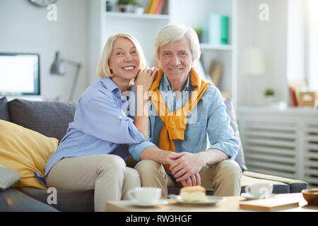 Portrait of happy mature couple posing together sitting on sofa at home, copy space Stock Photo
