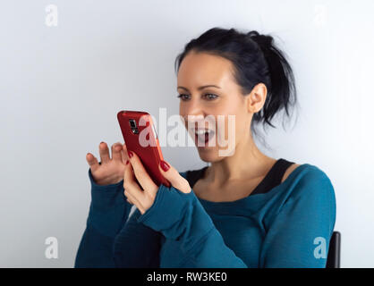 Young casual hipster woman holding and looking at cell phone reading unexpected sms news with a surprised and amazed facial expression, on white Stock Photo