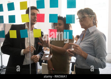 Serious multicultural business team discussing project plan with sticky notes Stock Photo