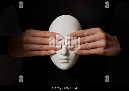 Woman's fingers close eyes of gypsum mask face on a black background. See no evil. Concept three wise monkeys. Stock Photo