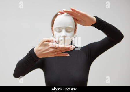 Woman's hands hold gypsum mask. Girl in a black jumper with plaster sculpture on a white background. Concept The masks we wear. Stock Photo