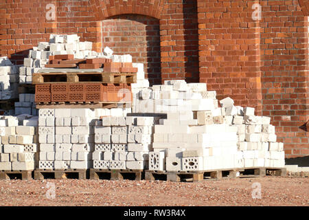 white and red building blocks, piled on pallets, in front of a red house wall Stock Photo