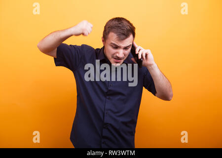 Young man in rage talking on mobile phone over yellow background. Shouting loud Stock Photo