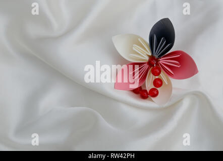 Beautiful colourful folded origami flower on a white shiny textile background Stock Photo