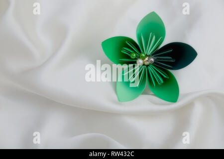 Beautiful colourful folded origami flower on a white shiny textile background Stock Photo