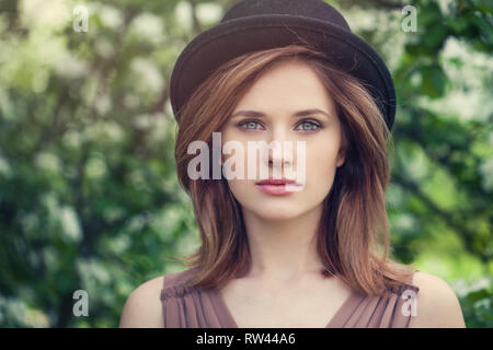 Woman face closeup outdoor portrait. Pretty girl in hat on greenery foliage background Stock Photo