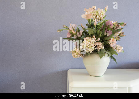Fake flowers in white vase on the table with purple wall background texture Stock Photo