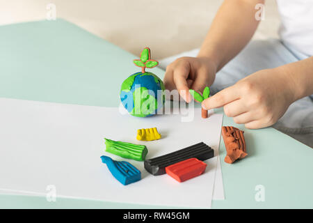 The child sculpts from plasticine the globe and trees. Layout of the planet in children's palms. Concept ecology. Stock Photo