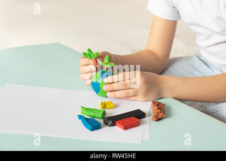 The child sculpts from plasticine the globe and trees. Layout of the planet in children's palms. Concept ecology. Stock Photo