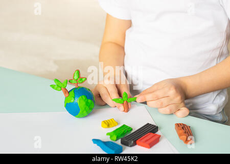 The child sculpts from plasticine the globe and trees. Layout of the planet in children's palms. Concept ecology. Stock Photo