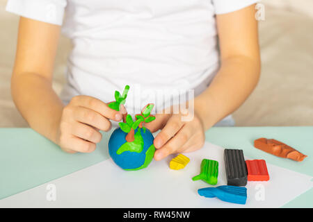 The child sculpts from plasticine the globe and trees. Layout of the planet in children's palms. Concept ecology. Stock Photo