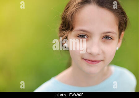 closeup portrait of happy smiling little caucasian girl in earrings and blue blouse on warm green background Stock Photo