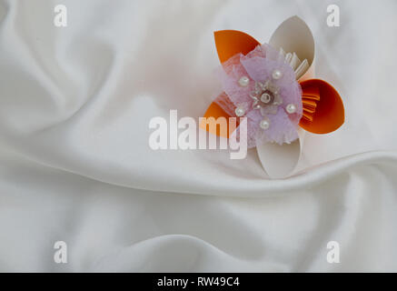 Beautiful colourful folded origami flower on a white shiny textile background Stock Photo