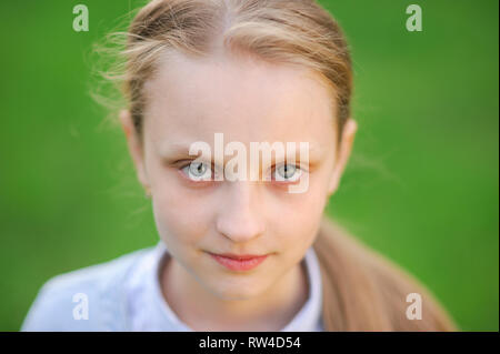 closeup portrait of beautiful blonde healthy little caucasian girl with clear skin on green outdoor spring background Stock Photo