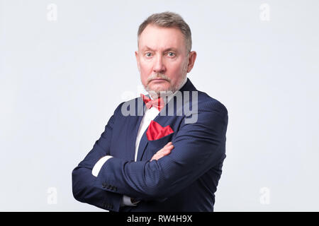 Senior businessman in blue suit looks at us on gray background. Stock Photo