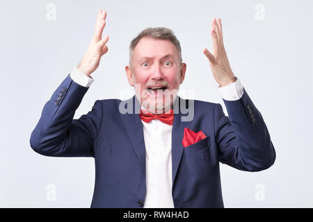 Oh no concept. Surprised, shocked man in blue suit holding hands up near head isolated on grey background Stock Photo