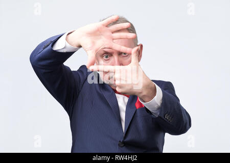 Handsome senior man looking through a frame formed by his hands. Attractive man make frame by fingers like he is looking for best shoot. Stock Photo