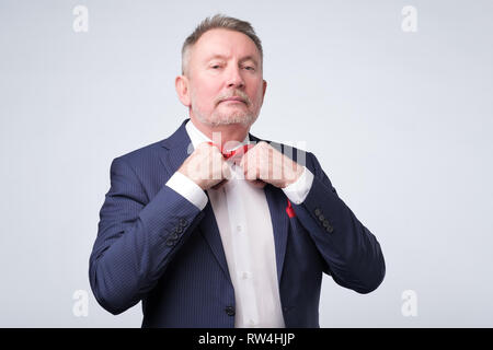 Handsome mature businessman in formal suit is adjusting his tie, on gray background Stock Photo