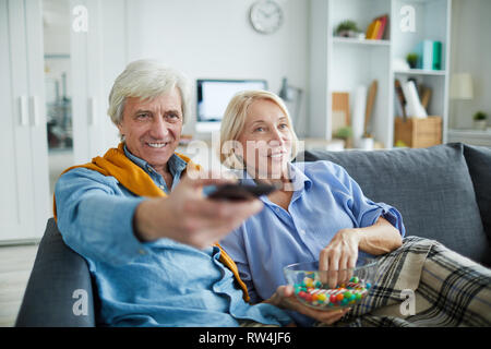 Portrait of contemporary mature couple watching tv at home and using remote control, copy space Stock Photo