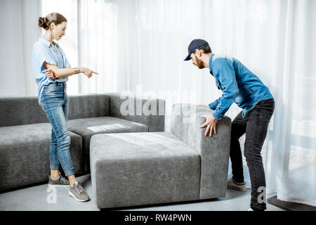 Delivery man mounting new sofa for a young woman client in the modern apartment Stock Photo