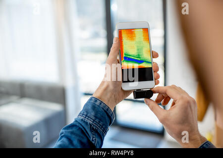 Man checking the house heat loss with thermovision camera and smart phone in the house Stock Photo