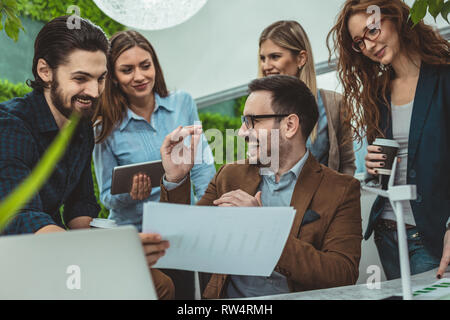 Smart qualified skilled young engineers are looking at the project of alternative energy with miniatures of windmill turbines at the table. Stock Photo