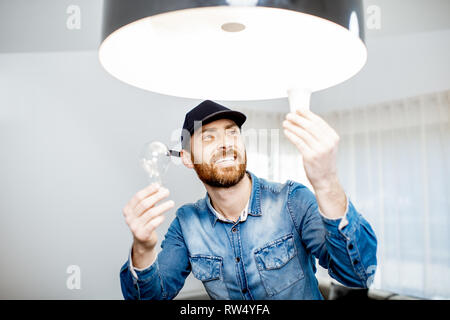 Handyman choosing between energy save and cheap incandescent lamp while changing light in the appartment Stock Photo