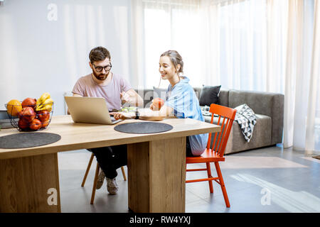 Young couple using laptop during the dinning time with healthy salad in the living room of the modern apartment Stock Photo
