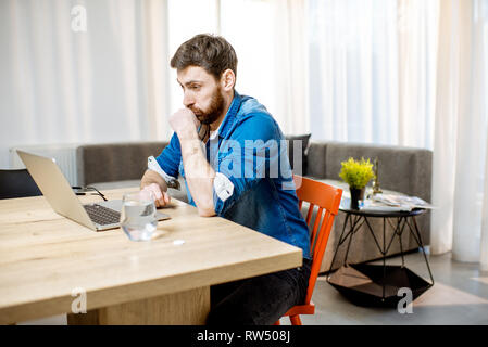 Hanndsome man feeling sick while working on the laptop at the table at home Stock Photo