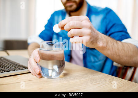 Man taking antipyretic or analgesic pills feeling bad while working on the laptop at home Stock Photo