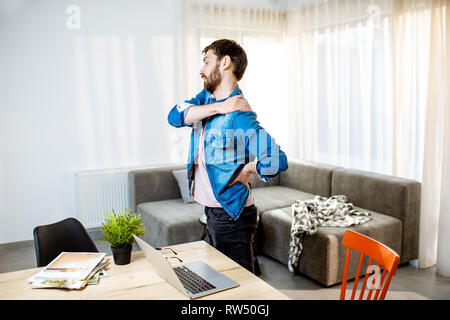 Man suffering from acute back pain while standing up from the working place at home Stock Photo