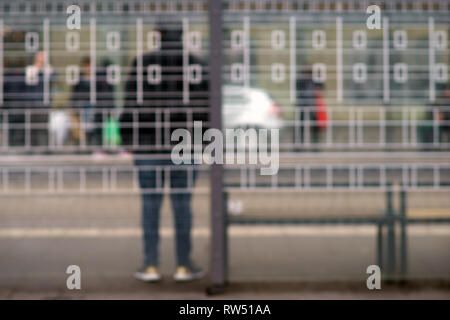 The new built glass shelter of a modern tram stop on a street with silhouettes behind blurred glass panes. Stock Photo