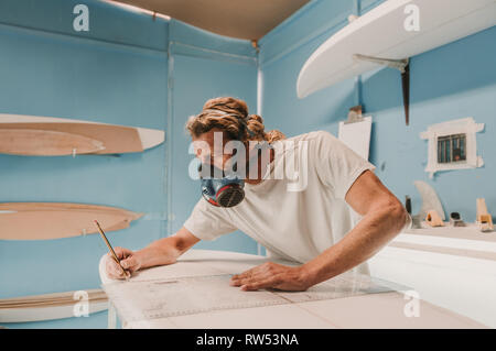 Side view of male in breather holding pencil and measuring surf board in workplace Stock Photo