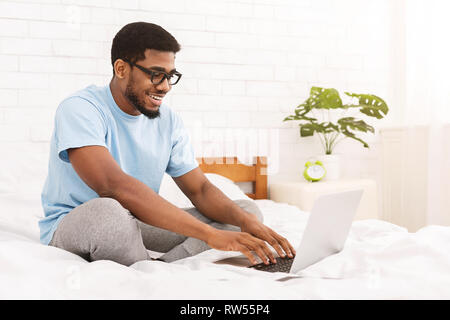 African-american programmer typing on laptop in bed Stock Photo