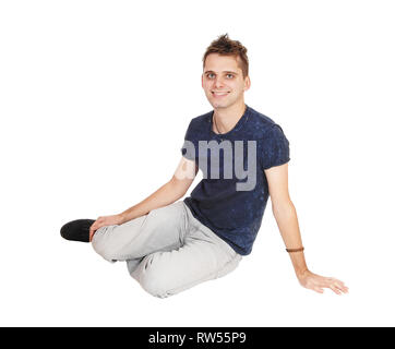 A handsome young man in gray jeans sitting on the floor in his gray jeans looking at the camera and smiling, isolated for white background Stock Photo