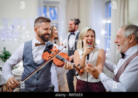 A young cheerful bride, groom and other guests dancing, singing and playing violin on a wedding reception. Stock Photo