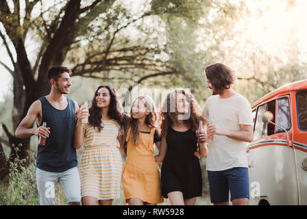 A group of young friends on a roadtrip through countryside, holding bottles and walking. Stock Photo