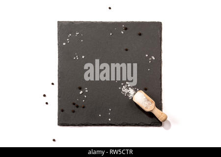 Isolated slate server on white background with space for text. Arranged salt crystals, peppercorns and wooden scoop. For restaurants, brochures, etc. Stock Photo