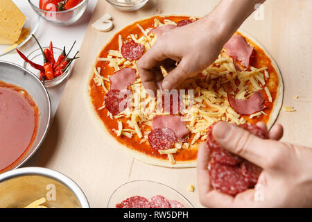 Chef cooking salami pizza, adding ingredients on it Stock Photo