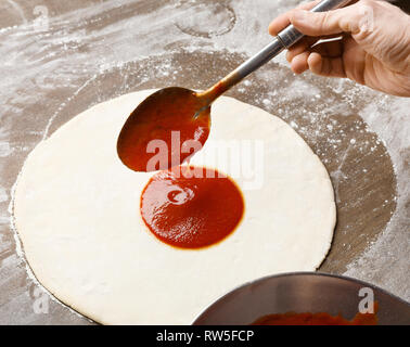 Adding sause on pizza base. Chef spreading tomato sauce Stock Photo