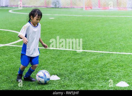 Little Asian girl is training in indoor soccer field Stock Photo