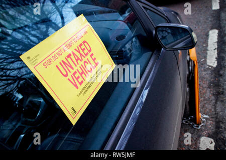 warning label and wheel clamp on untaxed vehicle car clamped on a street in the uk Stock Photo