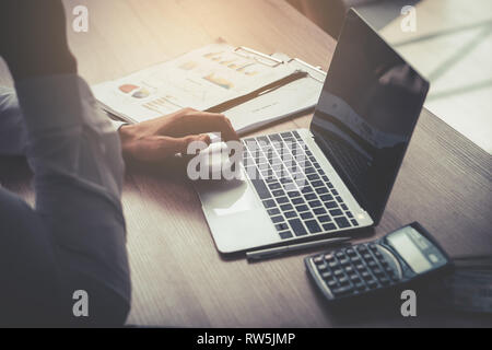 Business man is using computer on wooden table with calculator and financial accounting objects Stock Photo