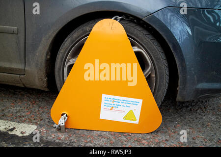 yellow wheelclamp on untaxed vehicle car clamped on a street in the uk Stock Photo