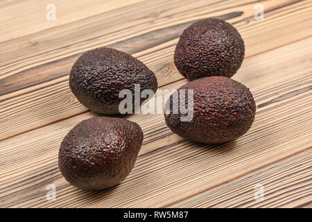 Four dark brown ripe avocados on wooden boards. Stock Photo