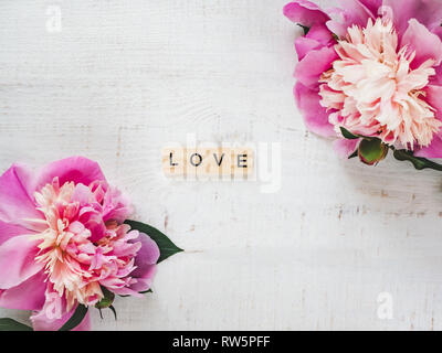 Colorful peonies and wooden letters of the alphabet in the form of the word LOVE on a white isolated background. Top view, close-up. Congratulations f Stock Photo