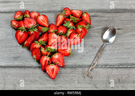 Top down view, heart made from strawberry pieces, silver spoon next to it, on gray wood desk. Stock Photo